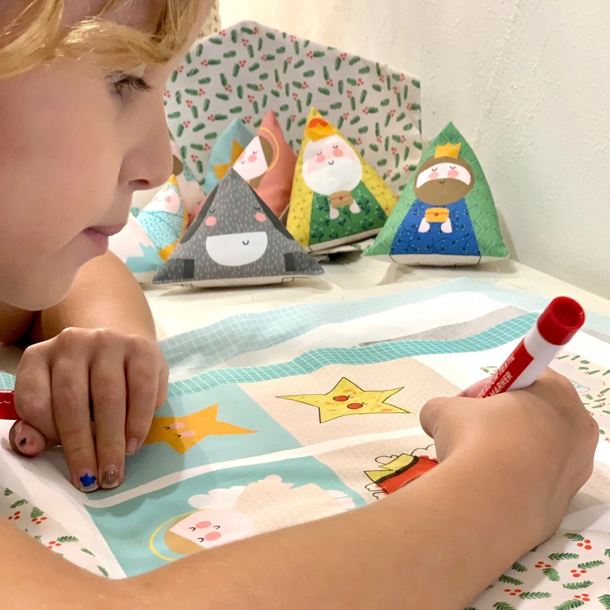 Niña pintando las figuras del pesebre de tela la blu antes de coserlas